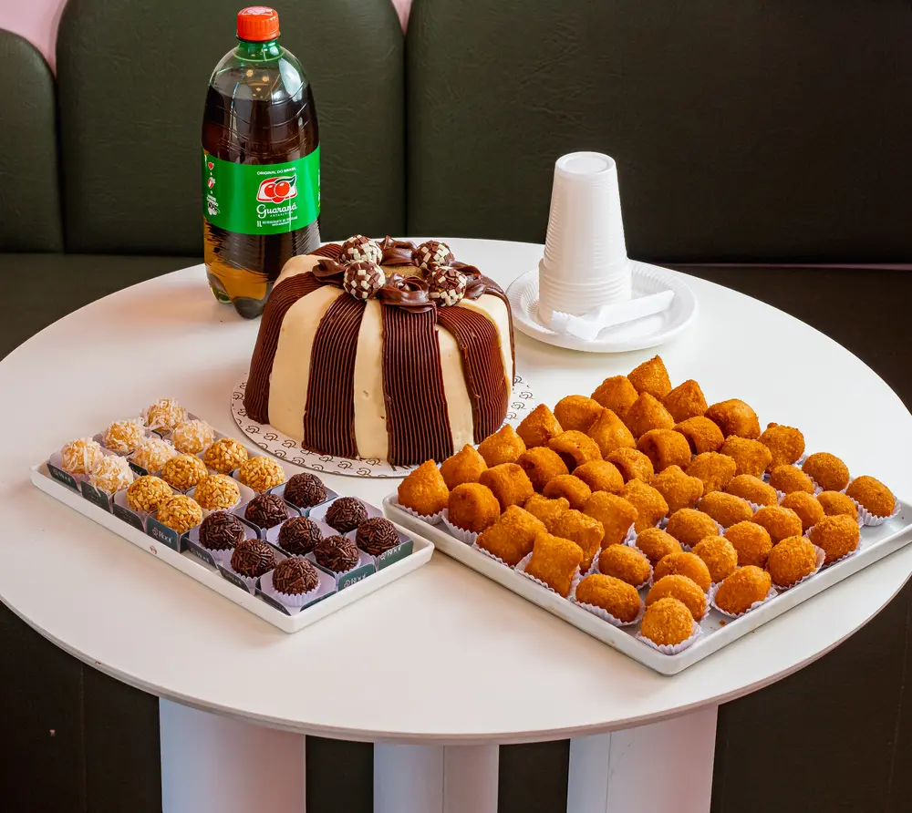 Bolo com cobertura de chocolate, brigadeiros, coxinhas e guaraná em mesa redonda